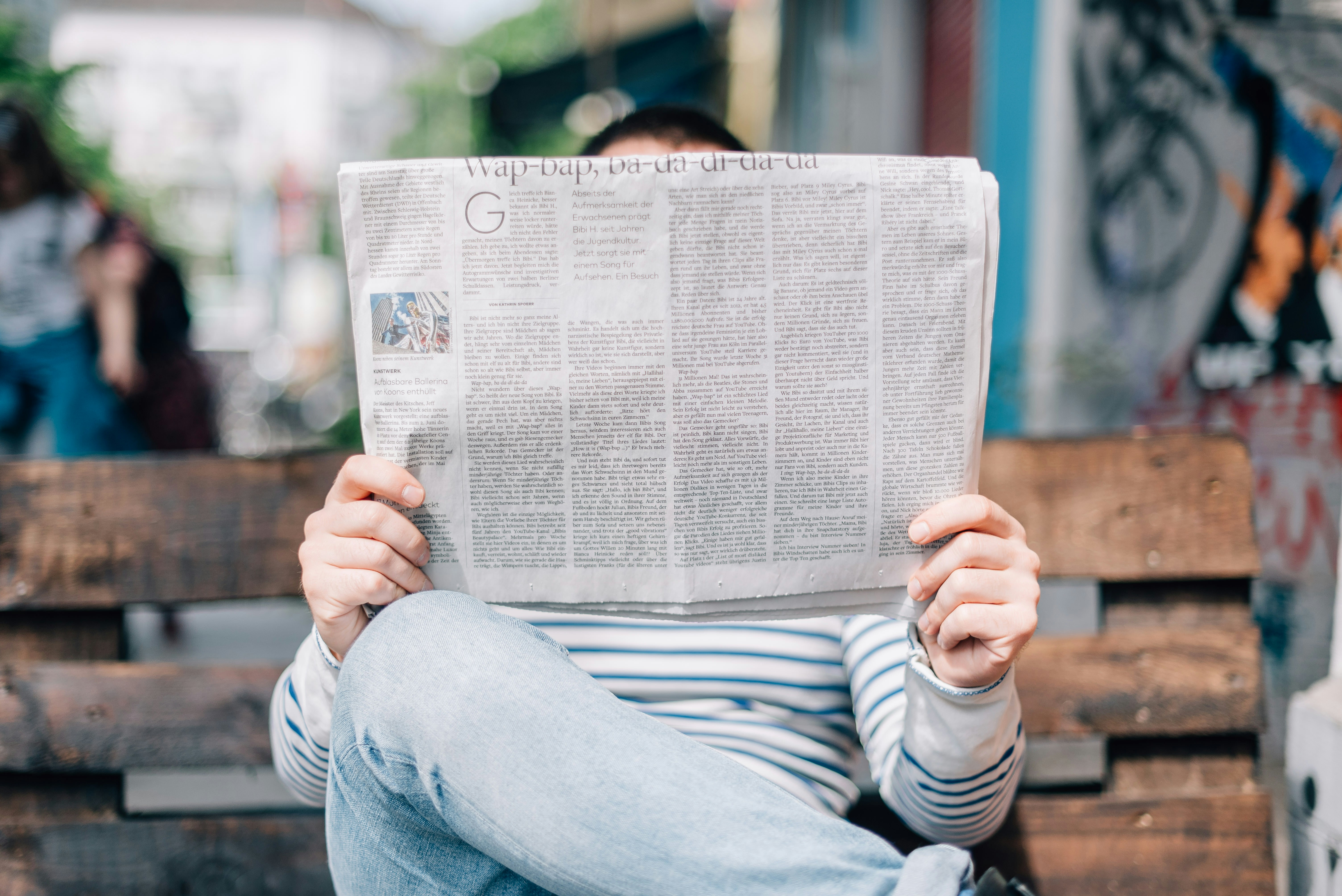Person sitting on a bench reading news.